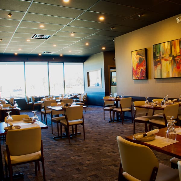 Empty restaurant dining room with set tables, modern art, and large windows.