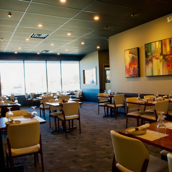 An empty restaurant dining room with set tables, modern art, and large windows.