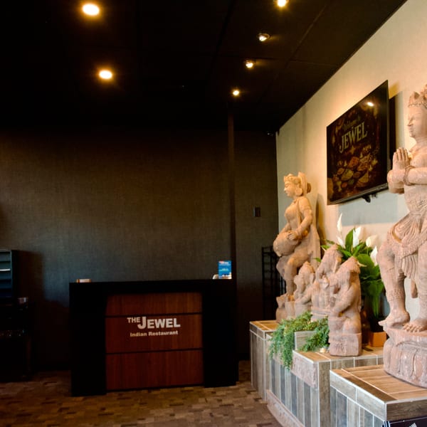 The Jewel Indian Restaurant's dark reception desk with a sign and statues of Indian deities.