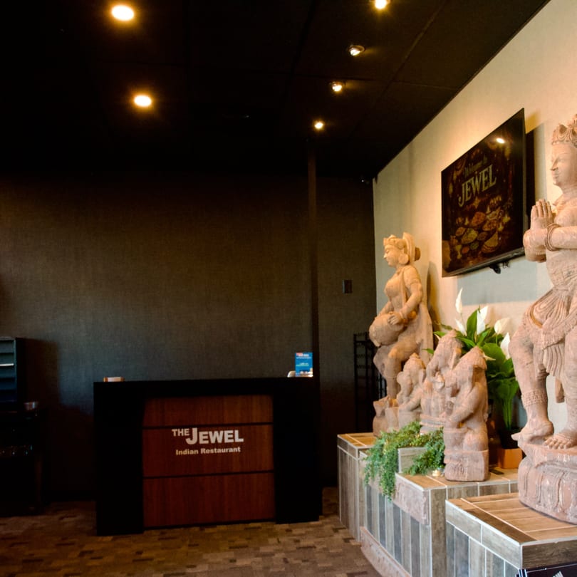 The Jewel Indian Restaurant's dark reception desk with a sign and statues of Indian deities.